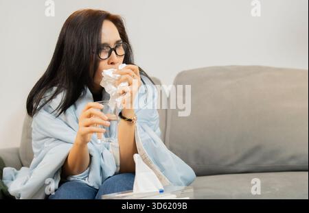 Femme asiatique couverture avec une couverture toux et a un mal de gorge boire de l'eau pour soulager un mal de gorge dans le salon à la maison. Copier l'espace. Banque D'Images