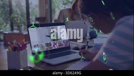 Écriture enfant portant des lunettes supérieures rayées assistant à la classe à distance à la table ordinateur portable AR icônes Banque D'Images