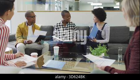 Discuter des collègues portant une veste et une salopette d'aviateur en examinant les documents sur le canapé gris et le dossier bleu Banque D'Images