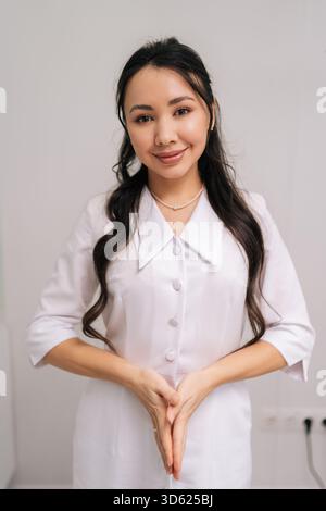 Femme asiatique souriante esthéticienne debout en uniforme blanc, représentant cosmétologue ou médecin confiant et professionnel offrant beauté et aestheti Banque D'Images