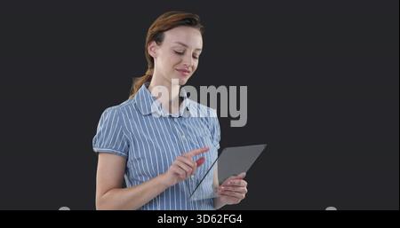 Femme adulte debout mi portant chemise rayée bleue tapant écran de tablette et souriant dans le studio Banque D'Images