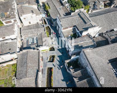 (NOTE DE LA RÉDACTION : image prise avec un drone) prise de vue aérienne du village de Xidi avec des bâtiments denses de style hui et une rue étroite avec des touristes et un ruisseau. Xidi Village est un ancien village renommé classé au patrimoine mondial par l'UNESCO. Il présente l'architecture exquise de style hui avec ses murs blancs, ses carreaux gris et ses sculptures complexes offrant un aperçu vivant de la vie rurale traditionnelle chinoise. En tant qu'exemple bien conservé d'anciens villages du sud de la Chine, Xidi attire de nombreux visiteurs du monde entier qui viennent apprécier son charme historique, son patrimoine culturel et ses paysages pittoresques. ( Banque D'Images