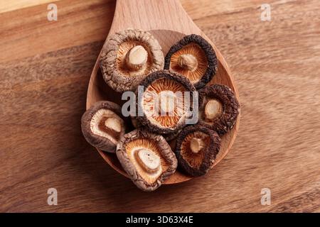 Champignons shiitake déshydratés écaillés biologiques séchés dans une cuillère en bois sur une table marron écologique. Vue de dessus Banque D'Images