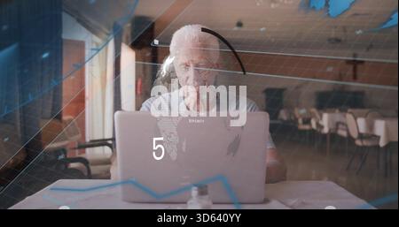 Homme senior travaillant se concentrant sur l'écran d'ordinateur portable à la salle à manger commune, avec superposition de carte numérique Banque D'Images