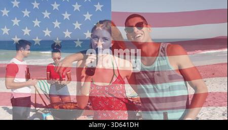 Dégustez un couple dans une robe rouge fleurie et un débardeur rayé sur la plage avec un gril et un drapeau superposé Banque D'Images