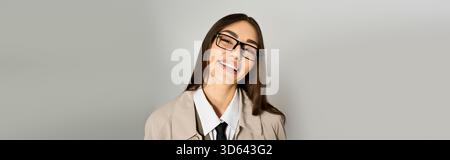 Une jeune femme heureuse pose avec un sourire amical, vêtue d'une tenue chic dans un cadre neutre. Banque D'Images
