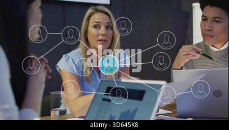 Femme principale portant chemisier parlant à l'équipe à la table en bois, superposition de réseau de papiers portables Banque D'Images