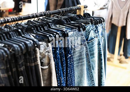 Vue rapprochée de différents jeans et pantalons accrochés à des cintres noirs sur un porte-vêtements dans un environnement de magasin de détail flou. Photo de haute qualité Banque D'Images