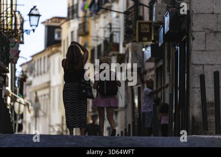 Lisbonne, Portugal - 18 juillet 2020 : vue de personnages se promenant dans une rue étroite et ensoleillée de Lisbonne, encadrée par des bâtiments anciens et la lueur accueillante Banque D'Images