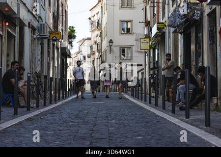 Lisbonne, Portugal - 18 juillet 2020 : vue sur une rue étroite et pavée bordée de bâtiments, où les piétons se promènent sous la douce lumière du jour, créant un Banque D'Images