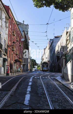 Lisbonne, Portugal - 18 juillet 2020 : vue d'un tramway jaune classique glissant le long des pistes à travers les rues étroites de Lisbonne, encadré par une construction colorée Banque D'Images