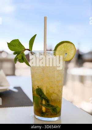Cocktail mojito glacé servi dans un grand verre avec des feuilles de menthe, de la glace pilée, de la tranche de citron vert et de la paille de papier sur une table de café en plein air majorque espagne Banque D'Images