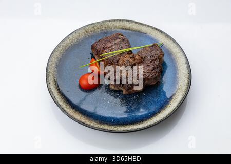 Steak de bœuf poêlé sur une assiette en céramique bleue avec tomates cerises, placage gastronomique minimal Banque D'Images