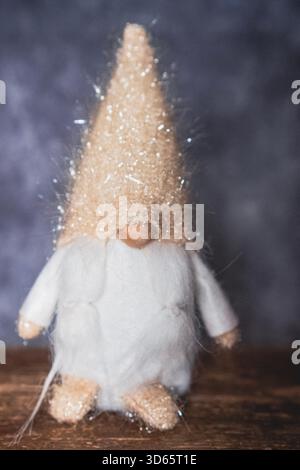 Gnome de Noël habillé de blanc et beige reposant sur une base en bois et un fond sombre Banque D'Images