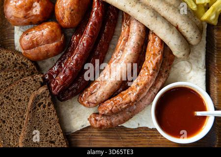 Un mélange de saucisses rôties et fumées avec des tranches de pain de seigle foncé et une sauce trempette. Banque D'Images