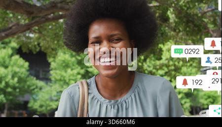 Femme souriante debout sous les arbres dans le parc, portant chemisier vert sauge et sangle bronzée, icônes d'application Banque D'Images