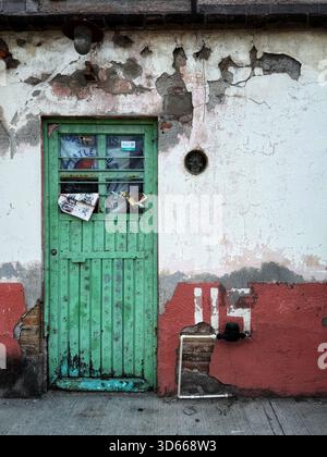 Porte en bois vert altéré avec peinture écaillée et vieux courrier sur un mur en stuc en détérioration dans un cadre de rue urbaine Banque D'Images