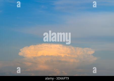 Une vue imprenable sur un nuage imposant cumulonimbus illuminé par la lumière douce du soleil contre un ciel bleu clair Banque D'Images