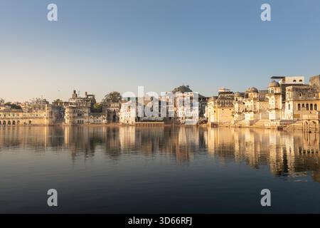 Vue matinale sur les Ghats de Pushkar reflétée dans les eaux calmes du lac, avec des temples historiques et des maisons qui brillent dans la douce lumière chaude du lever du soleil tôt. Banque D'Images