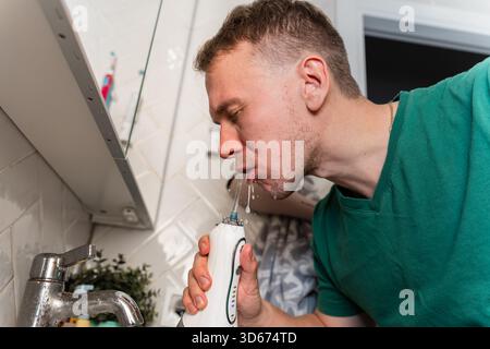 Un jeune homme se brosse les dents à l'aide d'un irrigateur avec un jet d'eau dans la salle de bain Banque D'Images