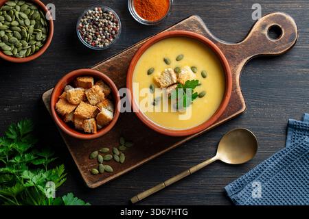 Délicieuse soupe à la crème de citrouille avec du pain cuit au four et des graines de citrouille dans un bol en céramique sur une table en bois, gros plan, vue de dessus. Concert de nourriture saine Banque D'Images