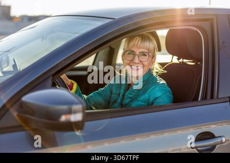 Pilote féminin mature souriant derrière le volant Banque D'Images