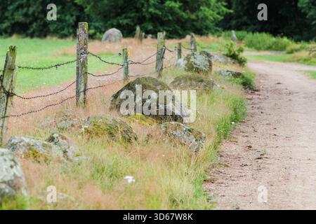Une route rurale de gravier. Une clôture faite de poteaux de bois et de barbelés, et de rochers couverts de mousse. Banque D'Images
