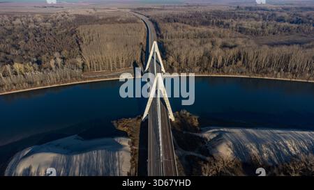 Vue aérienne du spectaculaire pont à haubans traversant le paysage, ses pylônes blancs et durs contrastant avec la rivière sombre et les bois automnaux, O. Banque D'Images