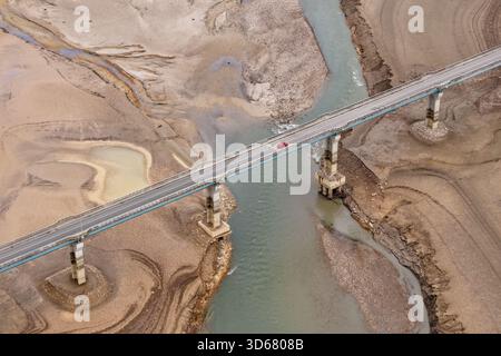 Vue aérienne d'une voiture rouge solitaire traverse le pont sur un lit de rivière sec, contrastant nettement avec le paysage desséché, Lisičići, Fédération de Bosn Banque D'Images