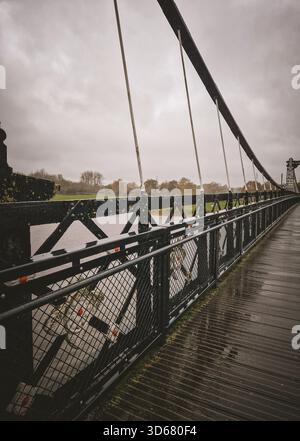 Une photographie atmosphérique et symétrique du pont historique Victorian Ferry Bridge (Stapenhill suspension Bridge) à Burton upon Trent, Royaume-Uni, sur un Wet, cl Banque D'Images