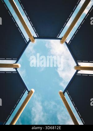 Une photographie abstraite frappante à angle bas regardant directement vers le haut à travers le centre d'une structure hexagonale de canopée (probablement un abri public ou un groupe de jeux Banque D'Images
