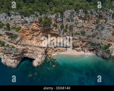 Vue aérienne des falaises accidentées embrassent une plage isolée où les eaux turquoises rencontrent le rivage, Konavle, Dubrovnik-Neretva County, Croatie. Banque D'Images