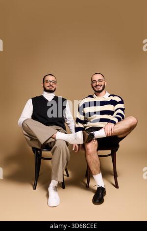 Deux frères jumeaux vêtus de tenues tendance posent en toute confiance dans un studio aux tons chauds. Banque D'Images