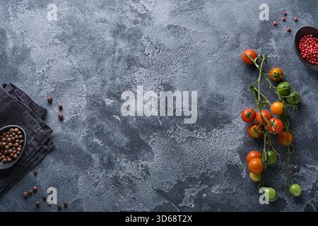 Branches de tomates cerises fraîches, serviette, poivre rouge et noir sur fond gris ancien. Fond de cuisine et maquette. Banque D'Images