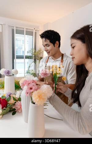 Un jeune couple arrangeant des fleurs colorées ensemble dans un cadre de maison confortable. L'homme, portant un tablier, aide la femme à créer un beau bouquet, shar Banque D'Images