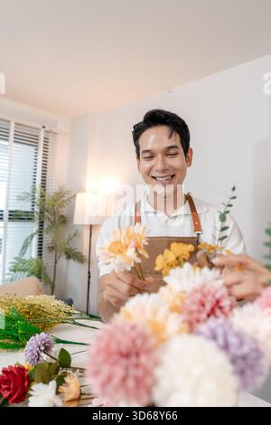 Un jeune couple arrangeant des fleurs colorées ensemble dans un cadre de maison confortable. L'homme, portant un tablier, aide la femme à créer un beau bouquet, shar Banque D'Images