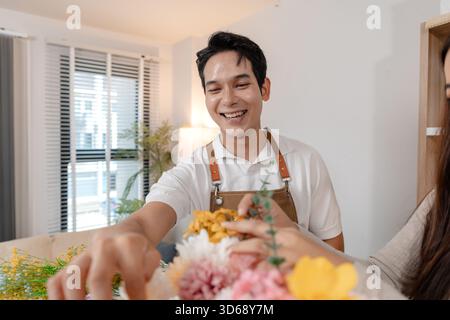 Un jeune couple arrangeant des fleurs colorées ensemble dans un cadre de maison confortable. L'homme, portant un tablier, aide la femme à créer un beau bouquet, shar Banque D'Images