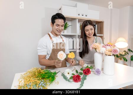Un jeune couple arrangeant des fleurs colorées ensemble dans un cadre de maison confortable. L'homme, portant un tablier, aide la femme à créer un beau bouquet, shar Banque D'Images