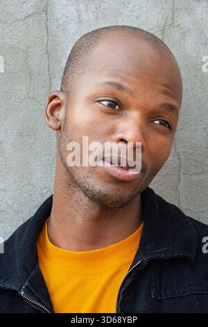 portrait d'un jeune homme africain à l'extérieur, tête rasée et vêtements décontractés, célibataire, Banque D'Images