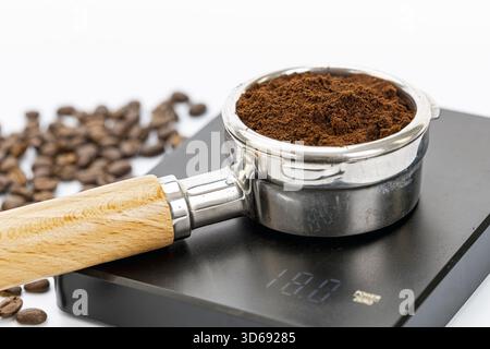 Un porte-filtre rempli de café finement moulu repose sur une balance de cuisine numérique affichant un poids de 18,0 grammes, avec des grains de café dispersés dans le Banque D'Images