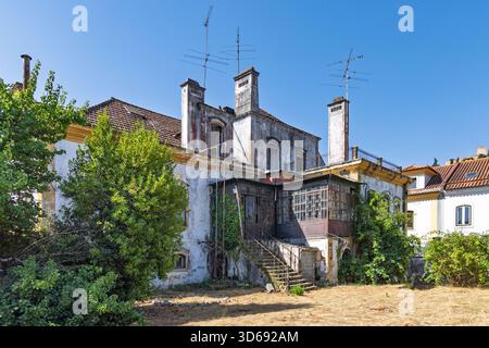 Une grande maison ancienne négligée à Tomar, Portugal, avec une végétation envahie, des façades altérées, de hautes cheminées, et un escalier extérieur. Banque D'Images