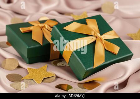 Deux boîtes-cadeaux vertes avec ruban jaune sur le fond de soie rose. Confettis ronds et étoiles jaunes sur le fond de soie rose. Banque D'Images