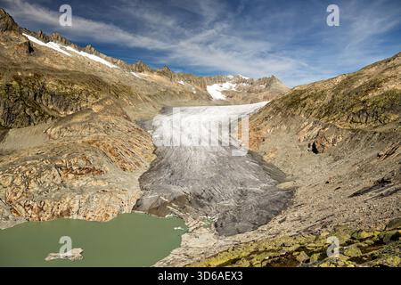 Le vaste glacier Rhône descend de façon spectaculaire entre les pentes accidentées des Alpes suisses, rencontrant un lac d'eau de fonte turquoise près de la route du col de Furka. Banque D'Images