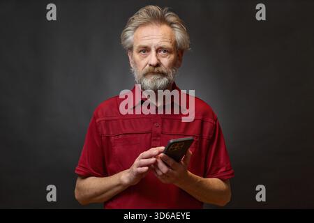 Vieil homme de plus de 60 portrait en studio avec smartphone sur fond noir Banque D'Images
