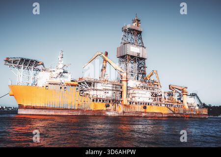 Navire industriel offshore massif avec structure de forage imposante, grues lourdes et charpentes métalliques complexes éclairées par une lumière chaude au-dessus de Ripplin Banque D'Images