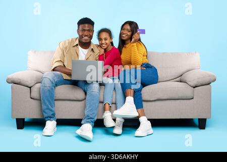 Happy Black Family apprécie les achats en ligne ensemble sur un ordinateur portable dans un salon confortable Banque D'Images