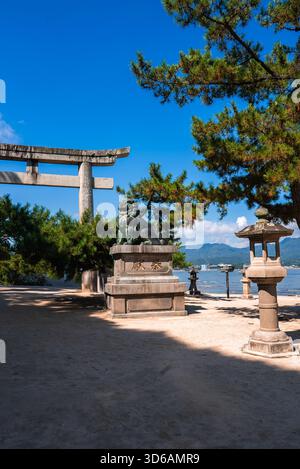 Komainu en pierre et lanternes près de la porte torii du sanctuaire Itsukushima, Miyajima Banque D'Images