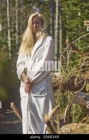 Cool femme attrayante debout grand portant peignoir à l'extérieur dans la nature dans la forêt à côté de stock de réserves de bois de chauffage, Holz vor der Huette haben, Banque D'Images