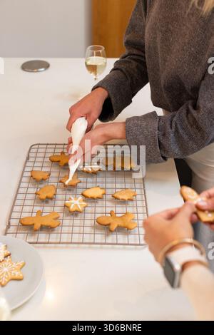 Sac à pâtisserie avec glaçage blanc sur les biscuits en pain d'épices sur le comptoir en pierre près du verre à vin Banque D'Images