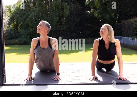 Amies seniors et adultes pratiquant le yoga sur le patio de la maison avec des tapis gris-noir Banque D'Images